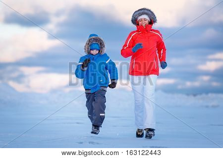 Cute little boy and his mother on icy beach, winter family holiday