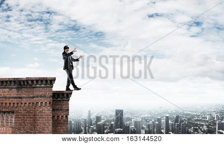 Businessman with blindfolder on eyes walking on building top