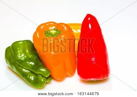 Green redyellow and orange peppers piled against a bright white background