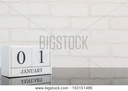Closeup white wooden calendar with black 1 january word on black glass table and white brick wall textured background with copy space selective focus at the calendar