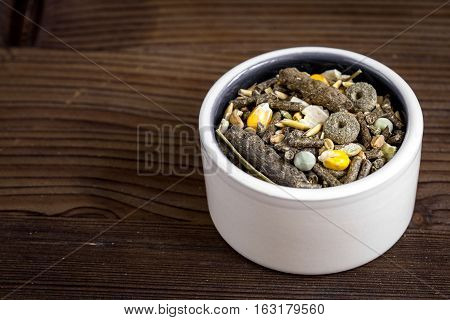 dry food for rodents in bowl on dark wooden background