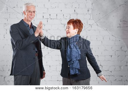 give a high five. Happy smiling old couple standing cuddling together isolated on white brick background. copy space