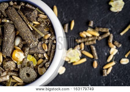 dry food for rodents in bowl on dark background top view.