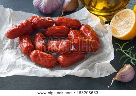 Small cervelat sausages and ingredients on black background