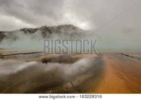 Along the turquoise color in the middle of the photo is the edge of Grand Prismatic Spring. The rest is buried in the steam from the spring. The mountains and clouds are reflected in the water.