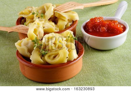 Arrangement of Delicious Meat Cappelletti with Herbs in Ceramic Bowls Tomatoes Sauce and Wooden Forks closeup on Green Napkin background