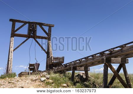 Old mining ore cart on trestle with head frame under blue sky.