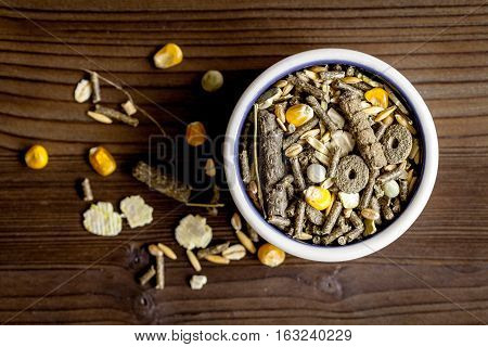 dry food for rodents in bowl on dark wooden background top view.
