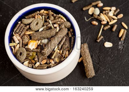 dry food for rodents in bowl on dark background top view.