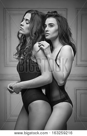 Two beautiful women in black erotic lingerie on white studio background. black and white photo
