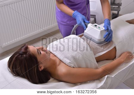 Pretty young woman getting cryolipolyse treatment in professional cosmetic cabinet