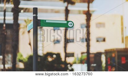 Narrow green waymark mock up with arrow inside of circle on street of summer city with blurred urban background with palms behind sunny day Barcelona Spain