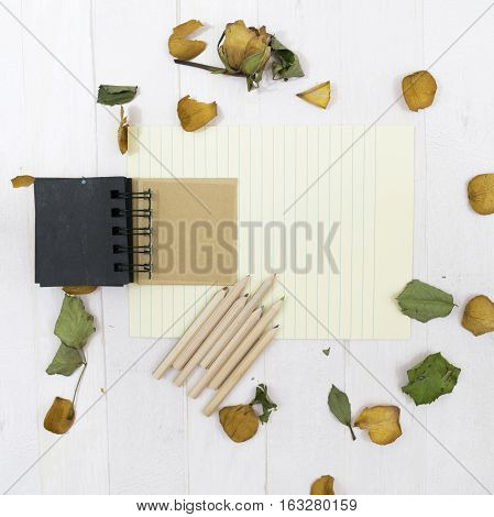 Open notebook on the white wooden background with dreid rose flowers, flakes and leaves. Romantic letter. Sheet of paper with lines