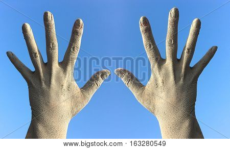Two female hands in the dirt and dust from the splayed fingers against the blue sky hands raised up