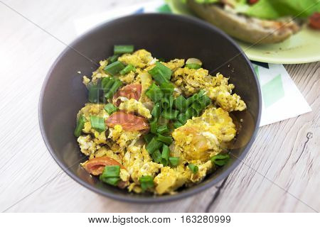 Scrambled eggs with chives and tomatoes in the brown bowl. Wooden background