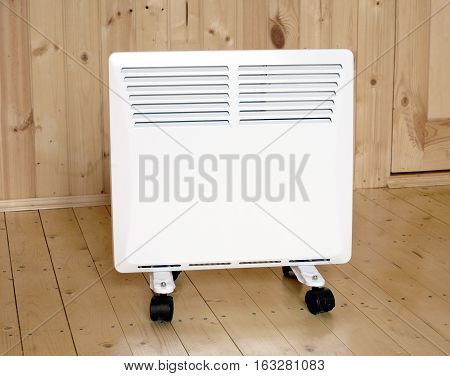 White electric convector heater with horizontal louvers in wooden house room