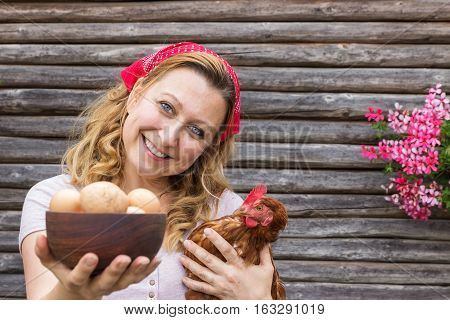Young peasant woman in front of a wooden background with eggs and a hen