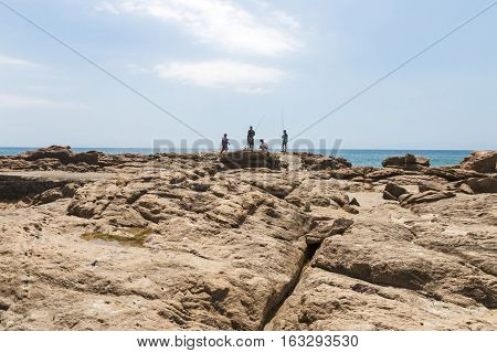 Four People Fishing On Rocks On Early Morning Beach