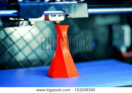 3D printer printing isolated volume triangular object red color on the basis of blue and black background close-up. Modern 3d printing technology