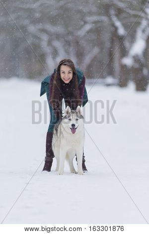 Happy and Smiling Caucasian Brunette Woman Playing with Husky Dog Outdoors in Park. Vertical Image