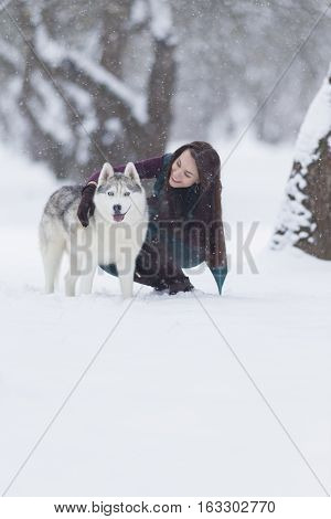 Happy Smiling Caucasian Brunette Woman and Her Husky Dog. Playing Outdoors in Winter White Forest. Vertical Image Composition