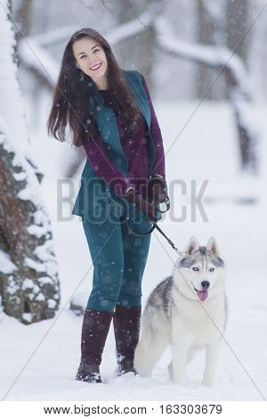 Home Pets Concept and Ideas. Happy Caucasian Brunette Woman and Her Husky Dog. Outdoors in Winter Forest. Vertical Image Composition