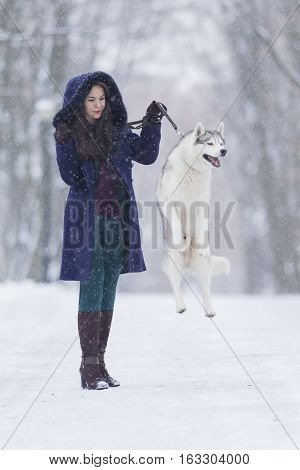Positive Caucasian Woman Airing Her Husky Dog. Jumping In Winter Forest Outdoors. Vertical Image