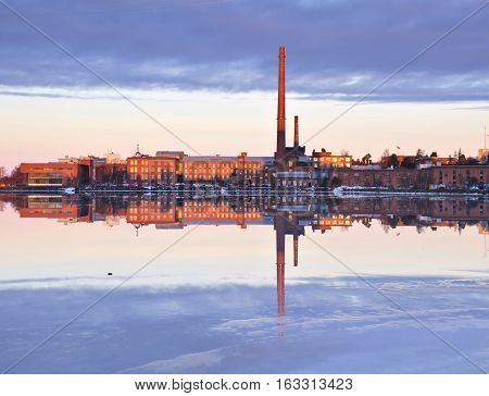 Old factory buildings by frozen sea. Reflection on ice and water. Architectural landscape.