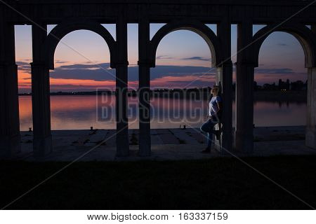 Young woman relaxing on the lake at sunset. Lonely woman enjoy watching sunset over the city lake in Bucharest