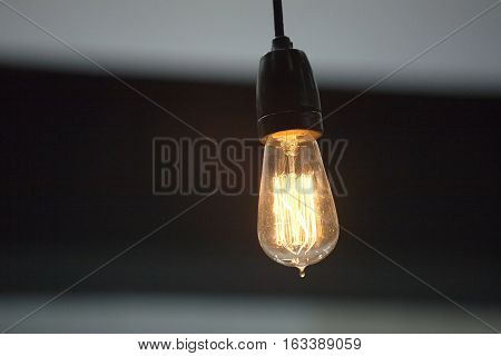 Lighting bulb in lamp-socket lights yellow against dark background closeup