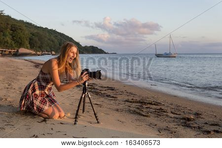 Young woman taking pictures on a sunset at a trokical island of Praslin in Seychelles