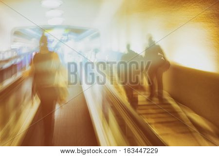Passengers on the escalator and go up the stairs in the station building in the rays of light. Blurry