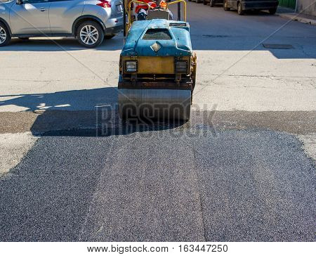 Worker on light vibration roller compactor at asphalt pavement works for road repairing