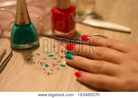 hands of a young woman who paints her nails red and green nail polish and decorate nails decorative sticker with a Christmas theme