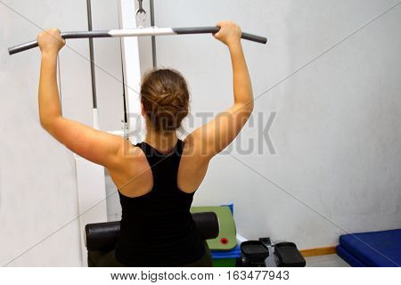 Woman at the gym. Working out her back muscles and arms with lat pulldown exercise machine.