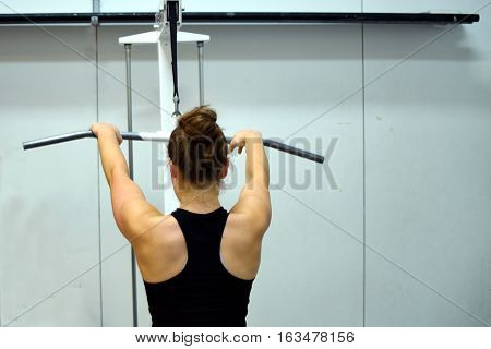 Lat pulldown at the gym. Woman working out her back muscles and arms.