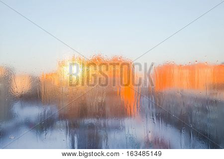 The icy glass of the window against the background of city buildings with the reflection of the sun