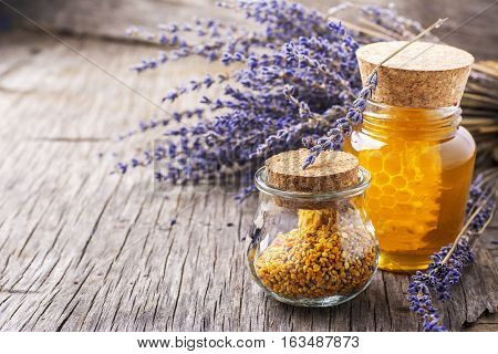 Arrangement of small glass jars with lavender honey, honeycombs and bee pollen with a bunch of dried lavender on dark wooden background. selective Focus