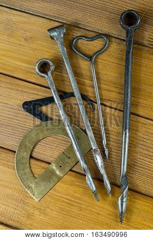 Several old gimlets, hand-tools for drilling holes in wood, calipers, protractor. Brown plywood background