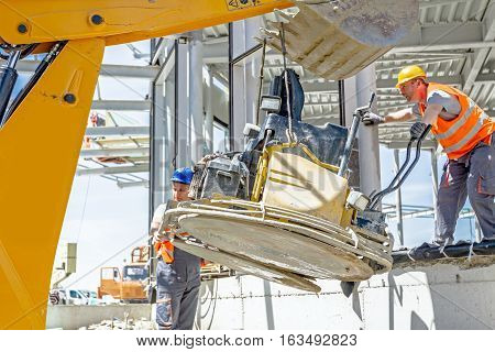 Zrenjanin Vojvodina Serbia - July 28 2015: Excavator is moving over building site with raised up back bucket a self leveling power trowel machine is hanging sander for smoothing surface to finish concrete slab.