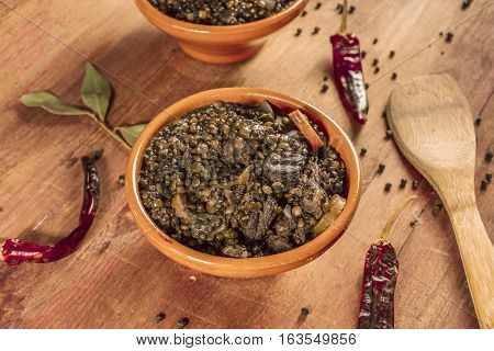 A photo of a lentil stew, shot on a dark wooden texture with bay leaves and peppers scattered around