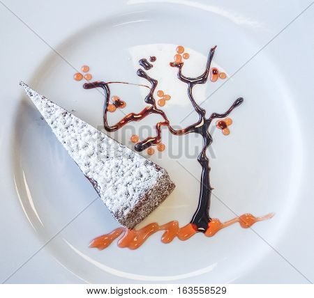 A typical neapolitan slice of Caprese cake made of chocolate and almonds with decorative tree made of peach jam and melted chocolate. Flat lay aerial view.