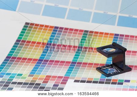 Magnifier or printer's loupe sits on a colorful CMYK test sheet in a pre-press workshop