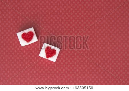 Sugar cubes with a red heart on one of them as background. Top view. Diet unhealty sweet addiction concept