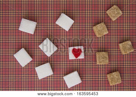 Sugar cubes with a red heart on one of them as background. Top view. Diet unhealty sweet addiction concept