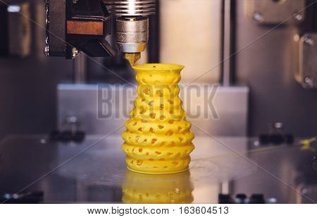 3D printer prints from the plastic figure closeup. 3D printer makes yellow model close-up on gray flat surface
