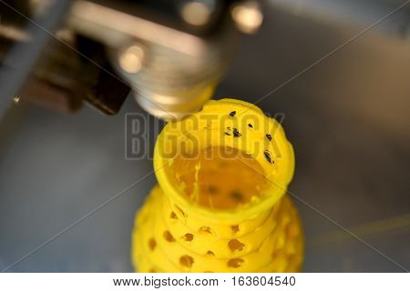3D printer prints from the plastic figure closeup. 3D printer makes yellow model close-up on gray flat surface