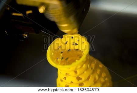 3D printer prints from the plastic figure closeup. 3D printer makes yellow model close-up on gray flat surface