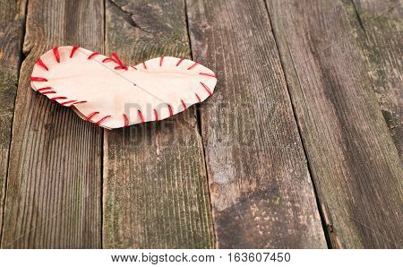 Self-made heart from paper on old boards. Edges of heart are sewed by a red thread boards gray not colored space free on the right