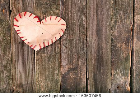 Self-made heart from paper on old boards. Edges of heart are sewed by a red thread boards gray not colored space free on the right